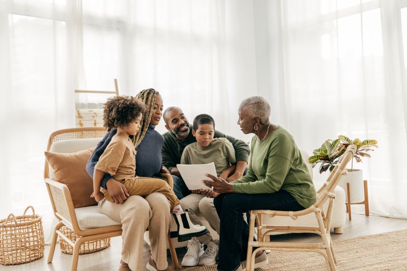 Family sitting in a living room while grandmother points to a document.