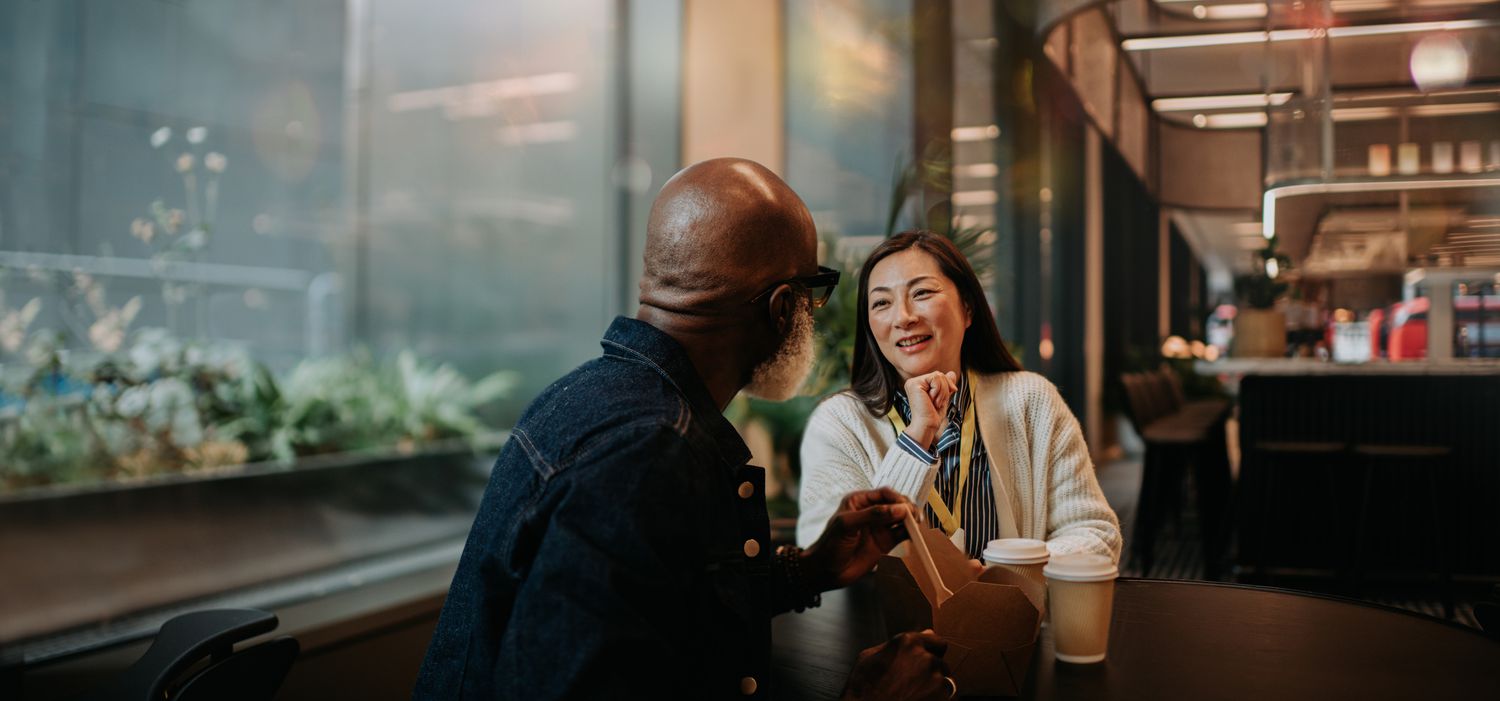 A man and woman look engaged in conversation as they have a casual meal in a cafe in the evening. 