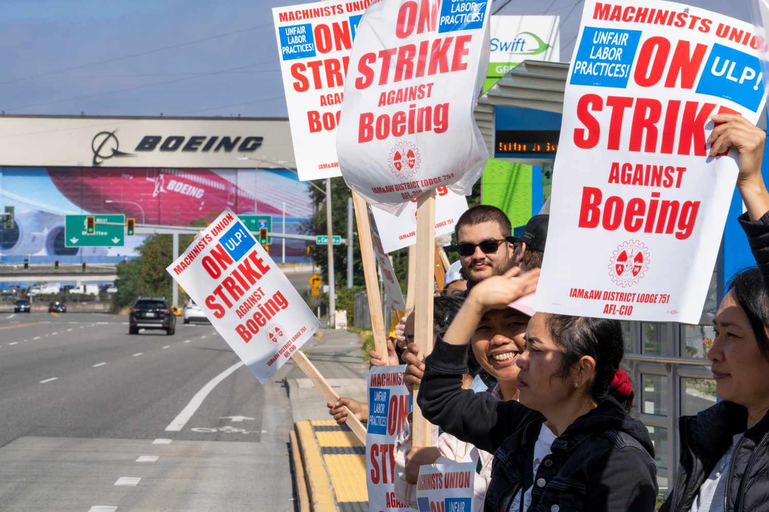 A group of Boeing workers stand on a sidewalk with picket signs during a strike.