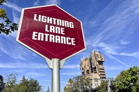 A red sign with the words "Lightning Lane Entrance" at a Disney theme park is seen in front of a blue sky
