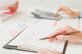 A close-up of people at a table reviewing financial documents, while one person uses a calculator.