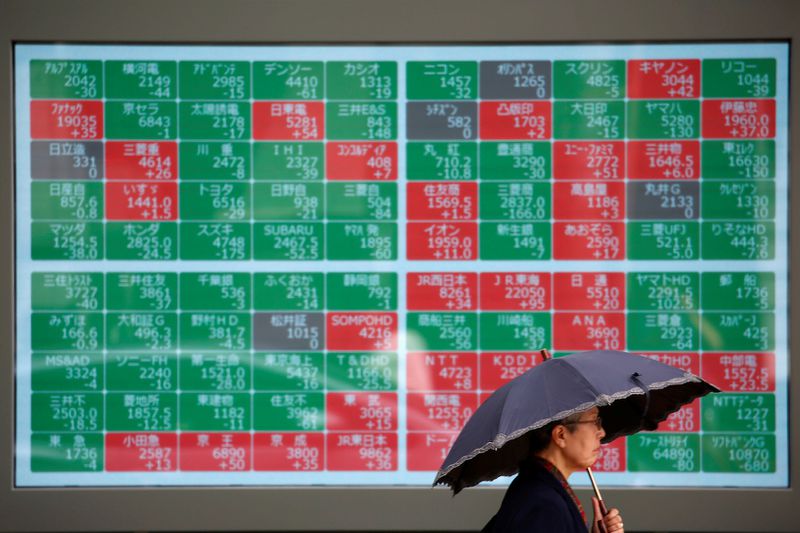 A passerby with an umbrella walks past a stock quotation board outside a brokerage in Tokyo