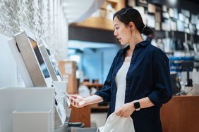 Woman using her phone to checkout a purchase at a self-checkout kiosk.