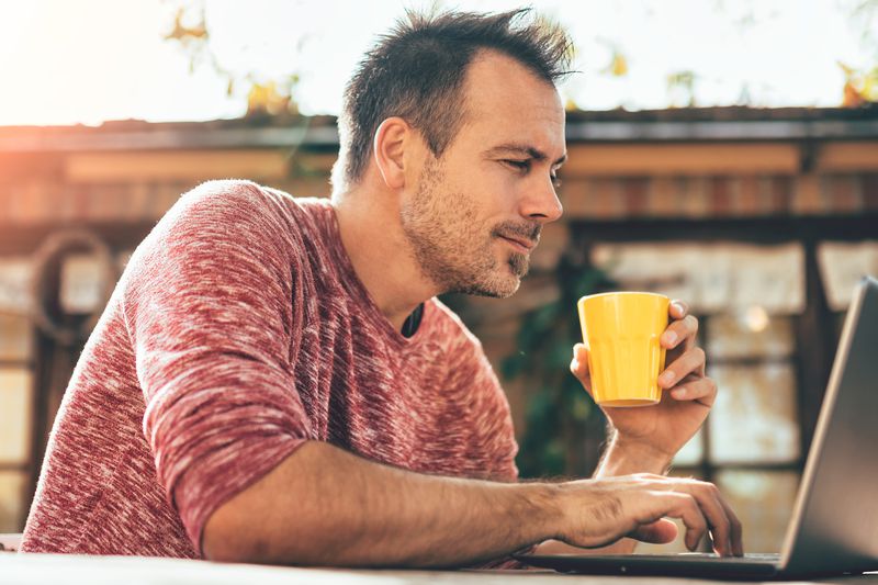A man drinking coffee, looking at his laptop