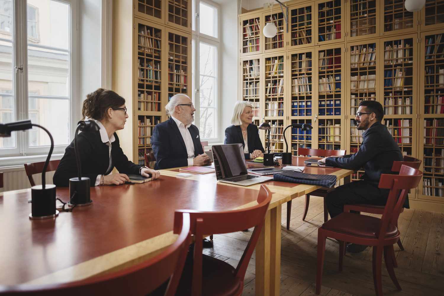 Mixed group of professionals sitting in meeting room with wood table and wooden bookshelves