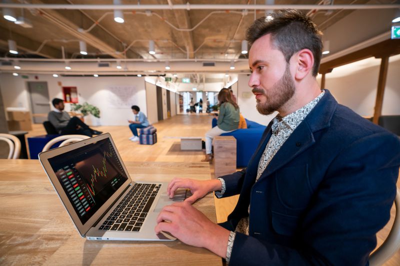 An options trader in a co-working space looking at a laptop exploring the values of various stock options and the time remaining on the contracts.