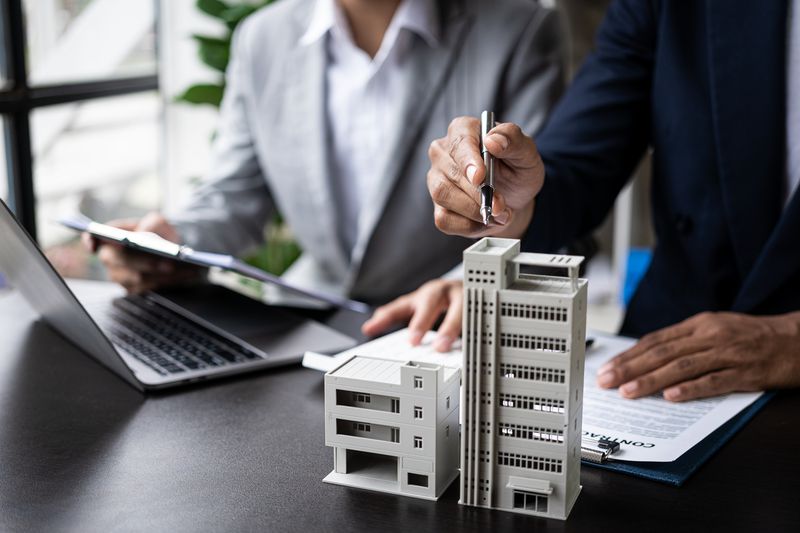 Two people look at the model of a building while reading over a contract
