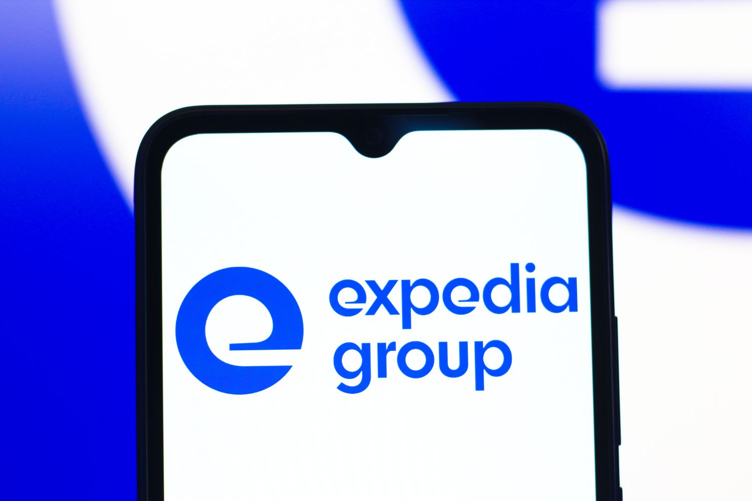 The blue Expedia Group logo is seen on a phone screen, with a blue and white background.