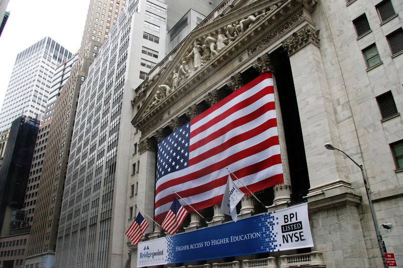 The exterior of the New York Stock Exchange on Wall Street, with a large American flag hanging from the facade.