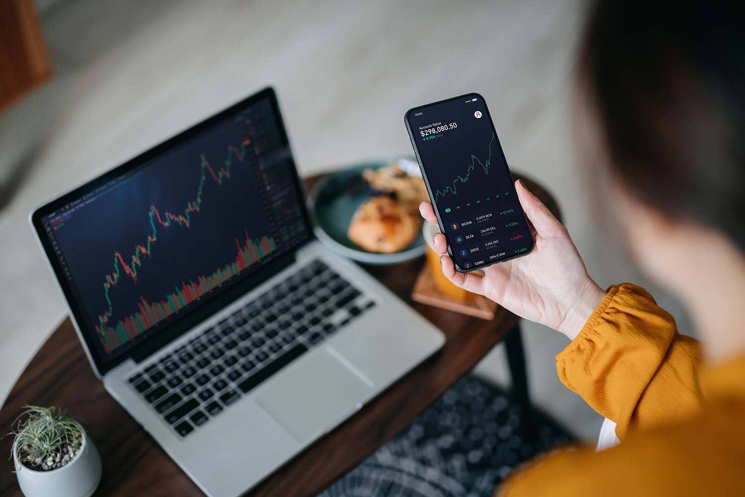 Over the shoulder view of Asian woman holding smartphone, analyzing investment trading data on crypto graph