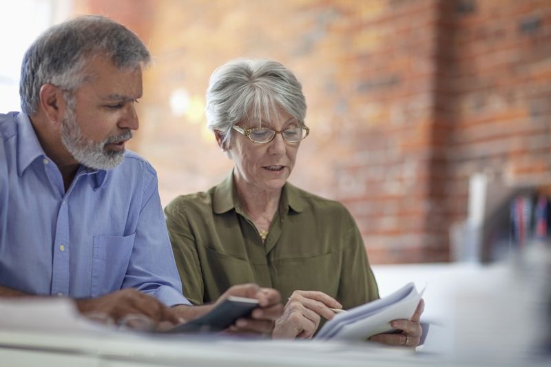 Couple in their 50s or 60s sitting at home and looking at mortgage documents and a calculator