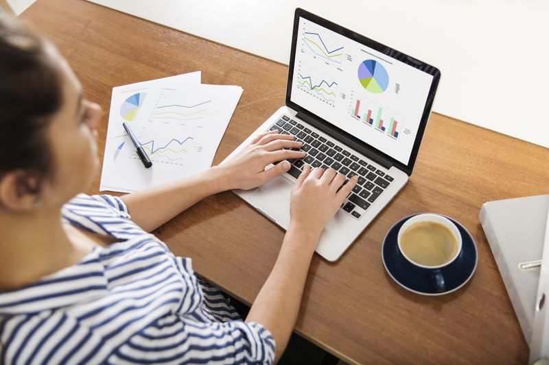 A young woman working on charts on her laptop at home.