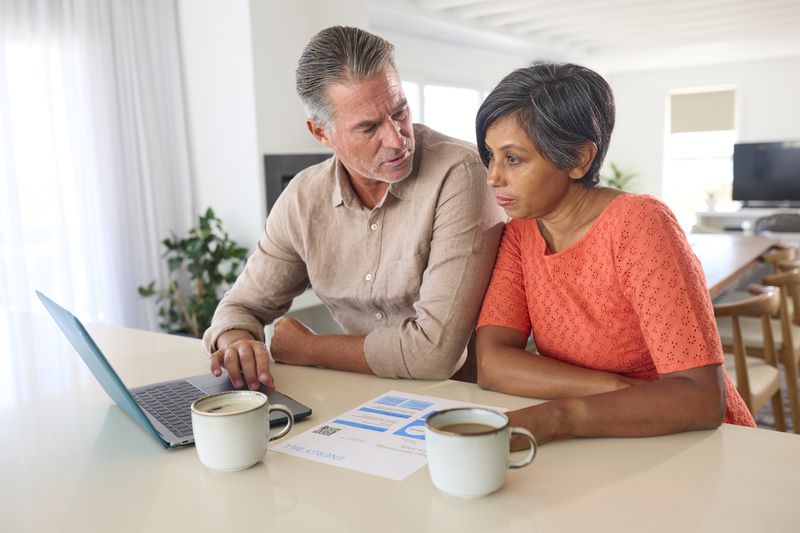 Couple in their 50s sitting in their kitchen and looking at mortgage rates on a laptop
