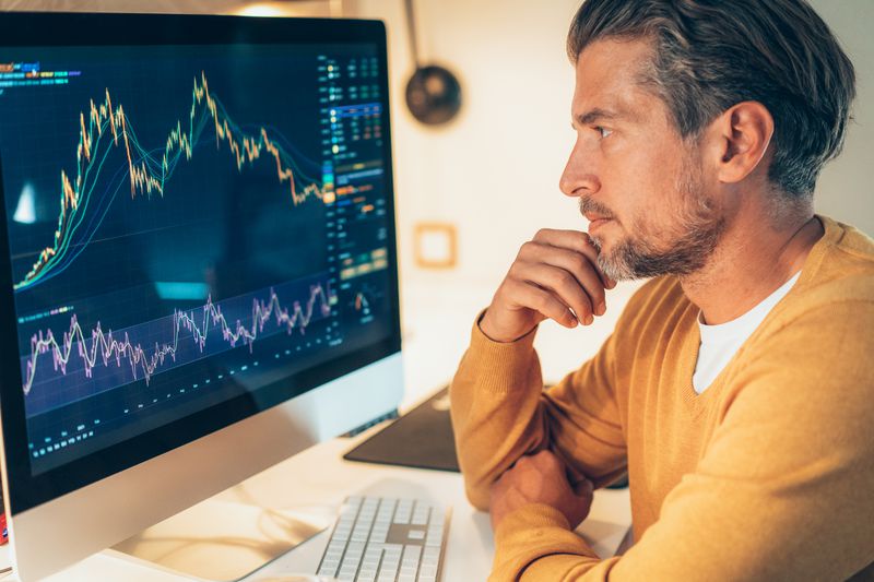 Man in a yellow jumper studying charts on a monitor.