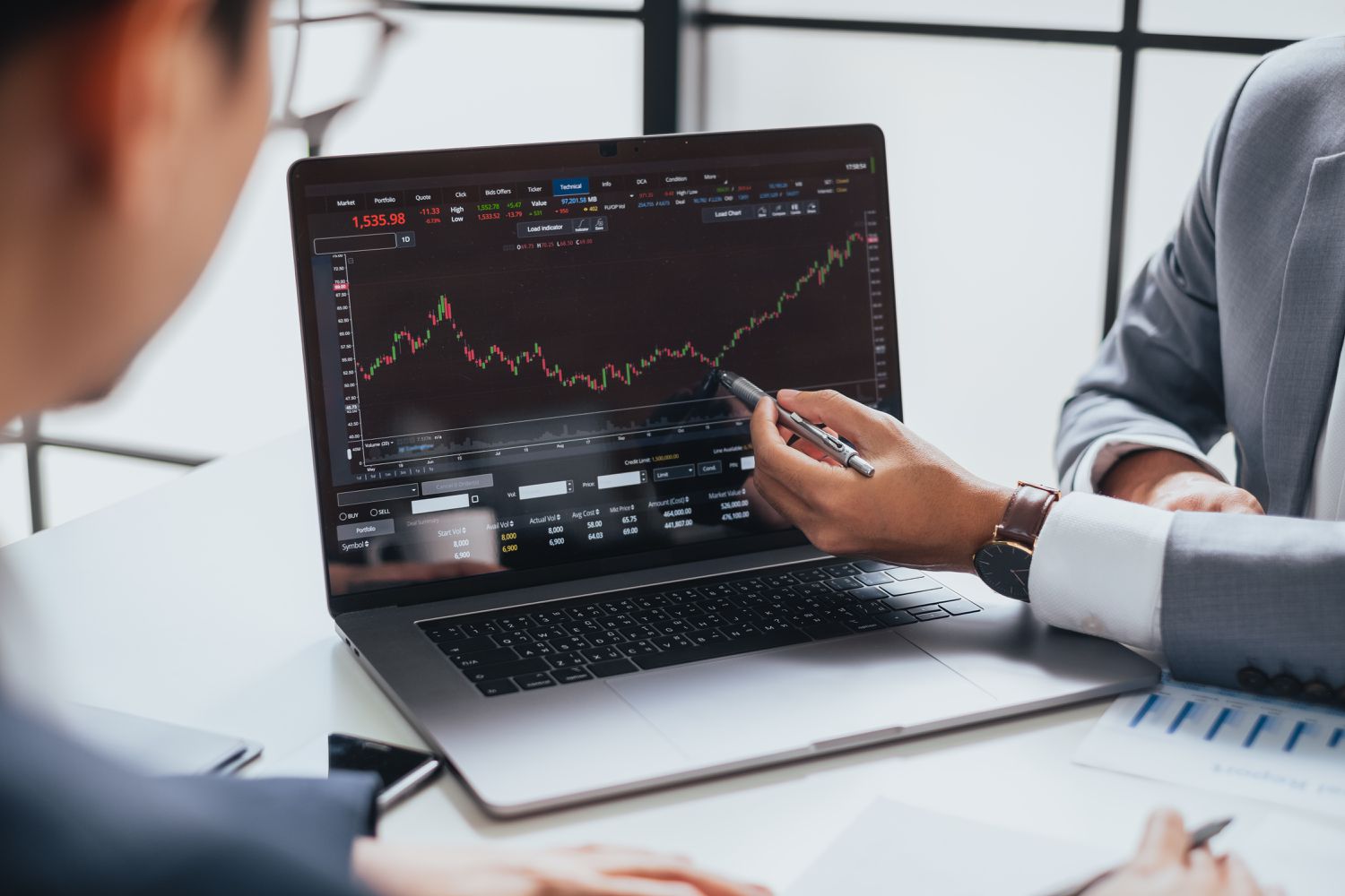 Man in business suit pointing with a pen to a computer with stock trading information