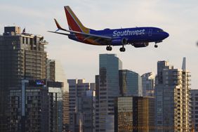A blue Southwest Airlines plane descends in front of several buildings.