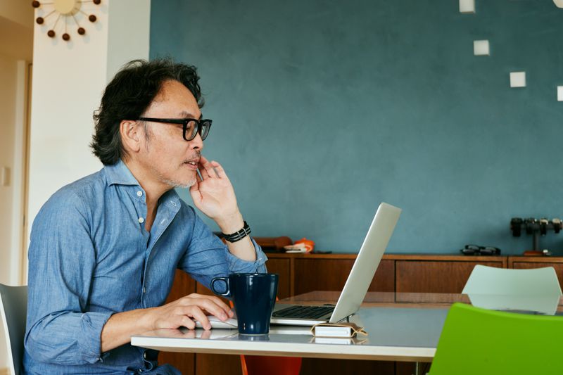 A man sits at a desk on a laptop with a coffee mug