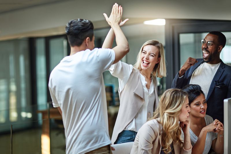 Group of colleagues giving each other a high five while using a computer together at work.