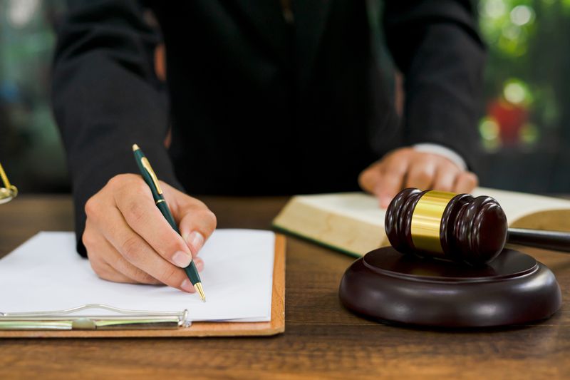 midsection of a lawyer writing on a clipboard with an open legal book and a gavel and block on the table