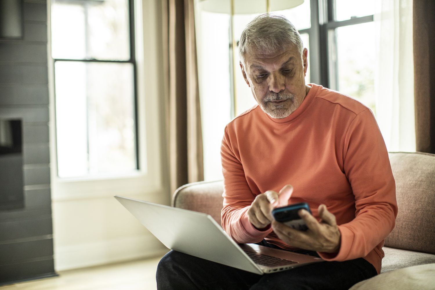 Senior man using laptop computer and smartphone at home