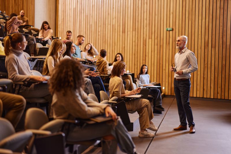 Senior professor talking in front of large group of his students during a lecture in amphitheater.