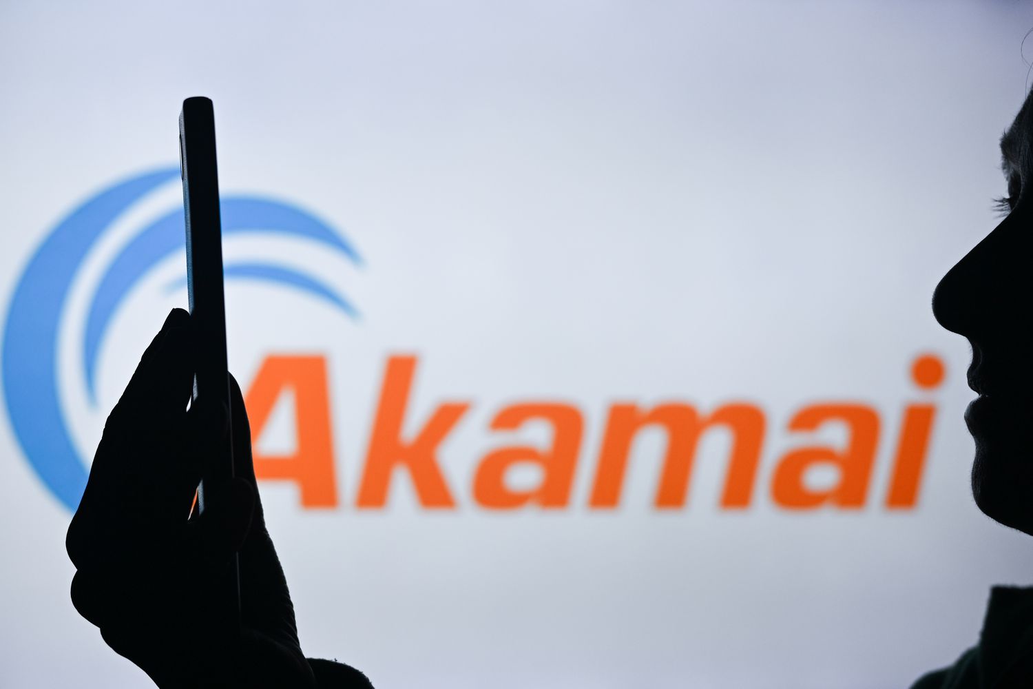 An image of a woman holding a cell phone in front of the Akamai Technologies logo displayed on a computer screen