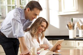 Couple in their 30s in their kitchen and looking happily at mortgage rates on a tablet