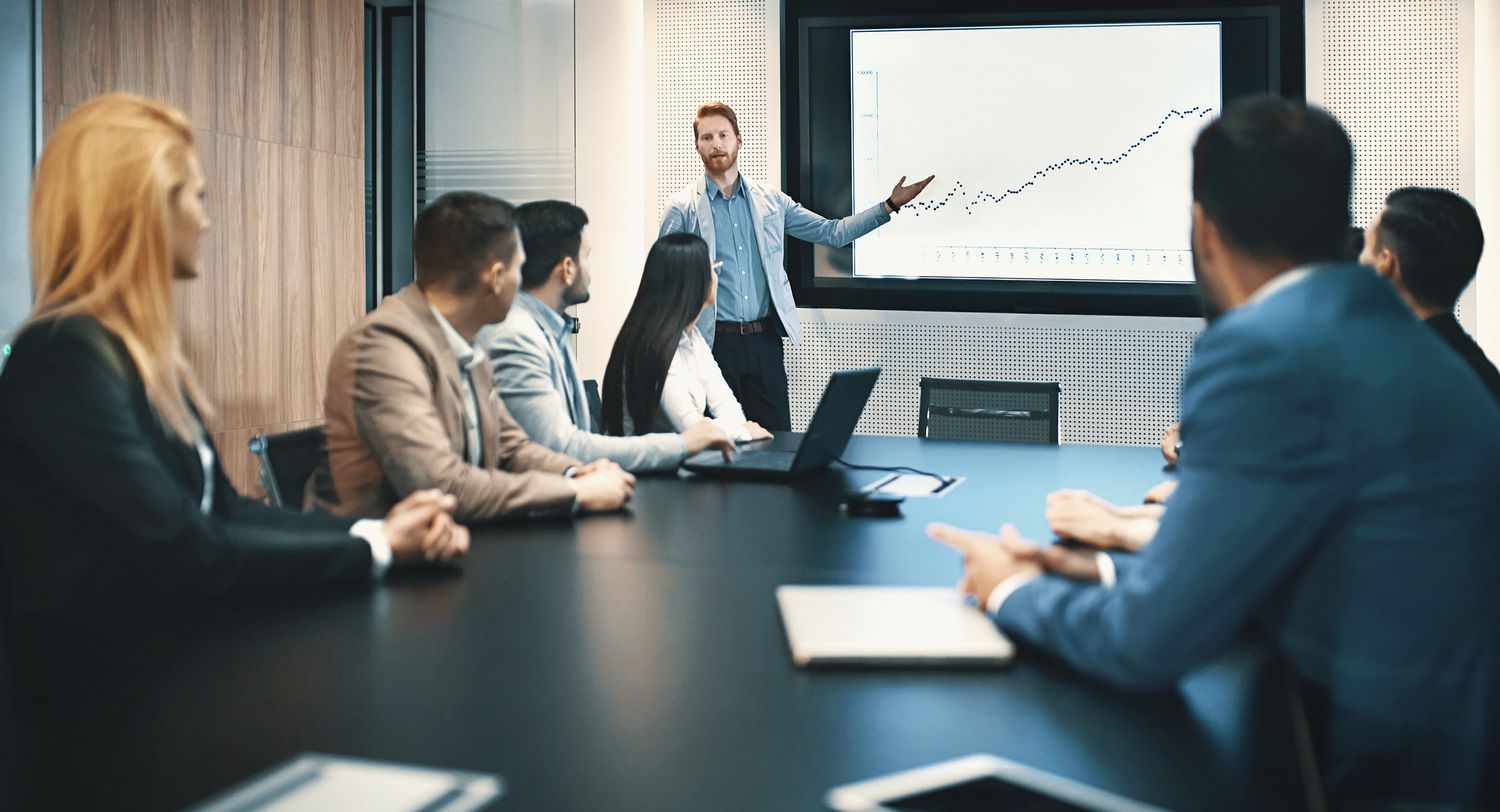 board room meeting with a man giving a presentation with a screen showing a line graph