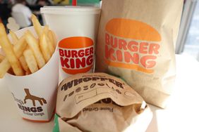 A Burger King bag and drink cup are seen on a table along with French fries and a Whopper cheeseburger.