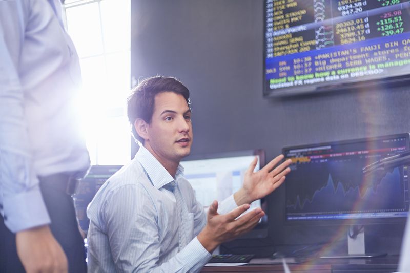 Young businessman in office having a discussion with monitors showing stock data