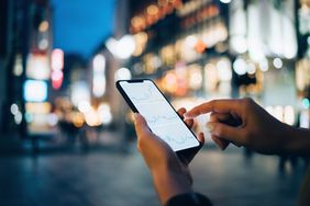 A close up of a person holding a smartphone and pointing at the screen displaying three financial charts. 