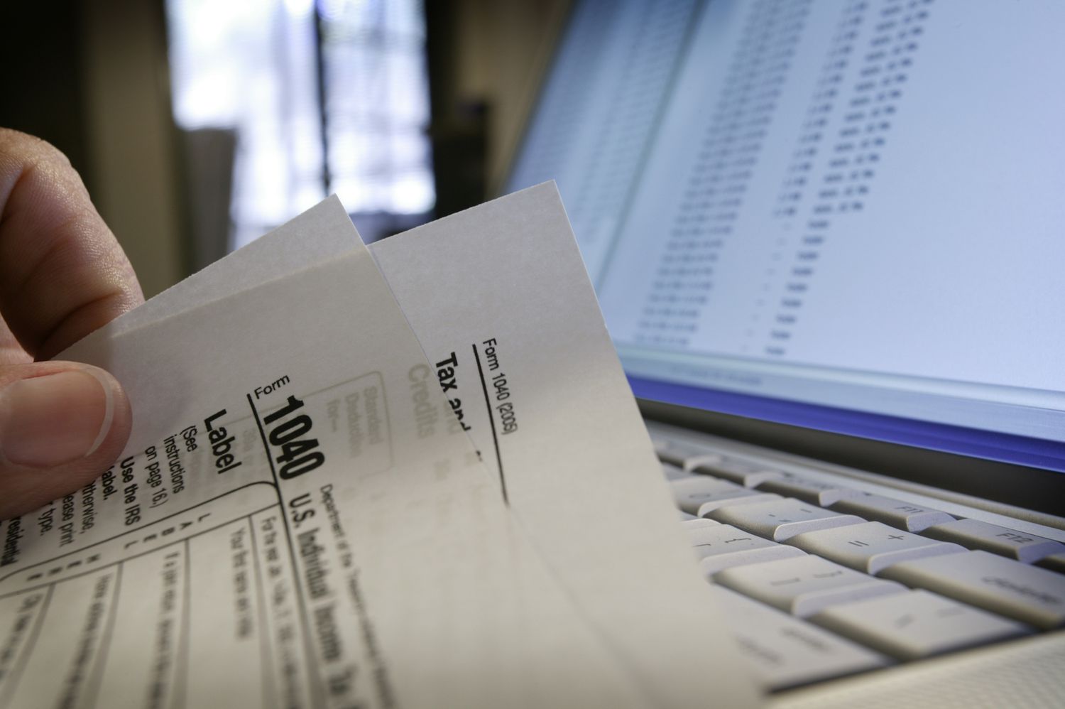 Close up of a man holding form 1040 at his computer, ready to file federal income taxes.