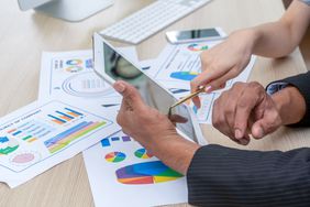 Two people point to stock portfolio information on a tablet.