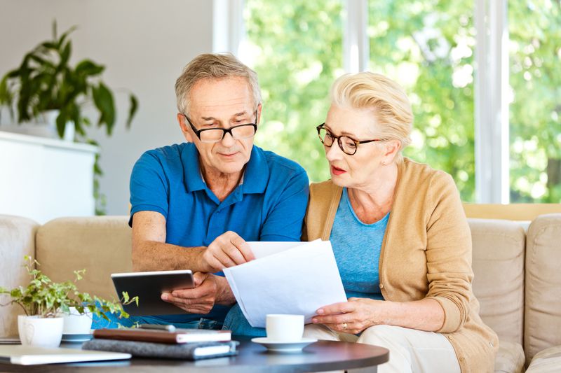 Older couple sitting on their sofa and looking together at bank statements and online rates.