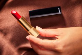 Close up of a person holding up the Chanel Rouge Allure Luminous Intense Lip Color Lipstick on a silk fabric background