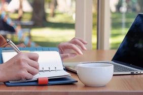 Woman taking notes in a notepad while working on a laptop.