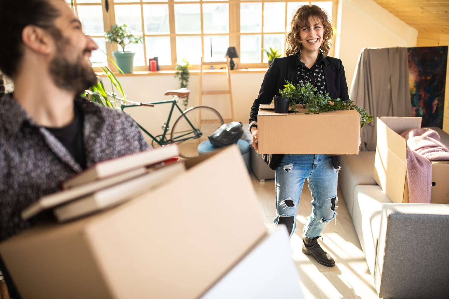 Happy young couple moving into their non-owner occupied apartment, carrying boxes and plants.