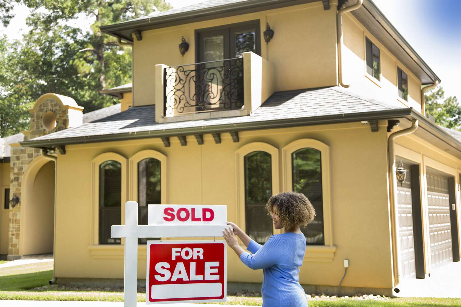 A real estate agent puts a sold sign sign in front yard of a home. 