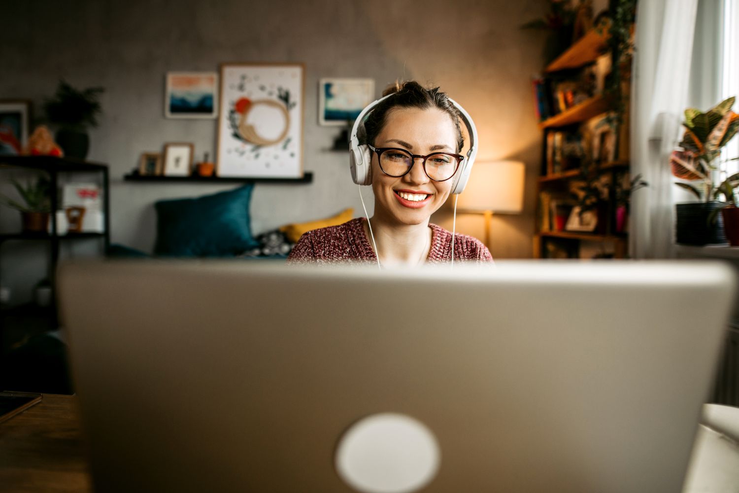 A young person wearing headphones sits in front of a laptop with a living room in the background. 