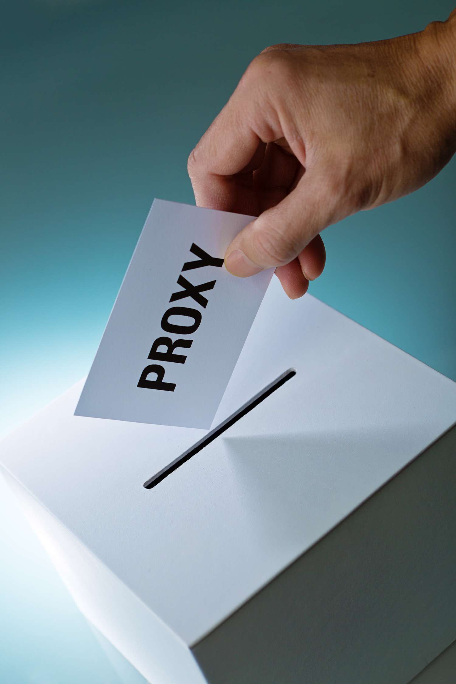 A hand dropping a proxy vote into a proxy ballot box. Photographed on white background.