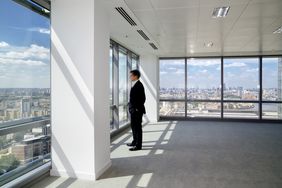 A business person standing in a high-rise building looking out the floor to ceiling windows. 