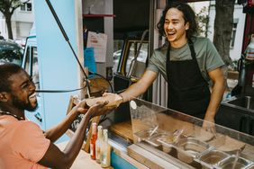 Food truck owner giving food container to laughing customer