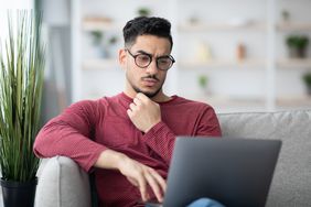 Young man on his living room sofa looking seriously at something on his laptop