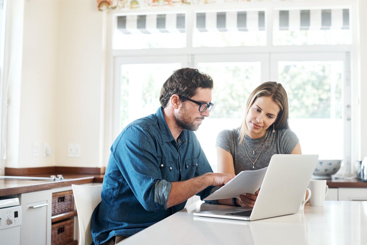 A man and a woman sit at the kitchen counter looking at papers and a laptop