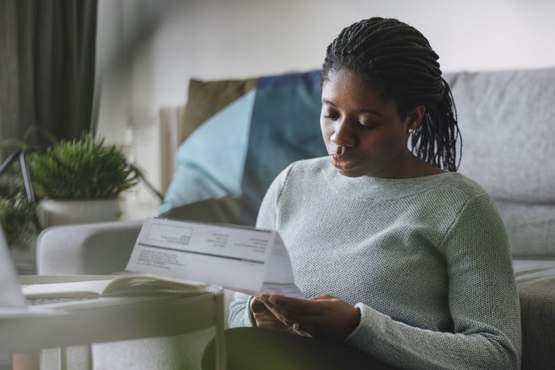Young woman reading a paycheck statement while sitting on the floor leaning on her couch