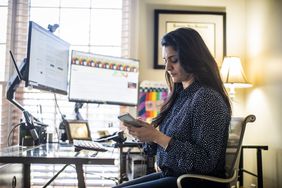 Woman reviewing a cell phone and screens in a home office
