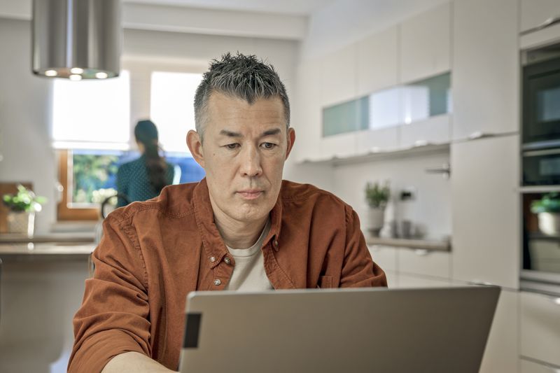 Mature man working on laptop while sitting in kitchen.