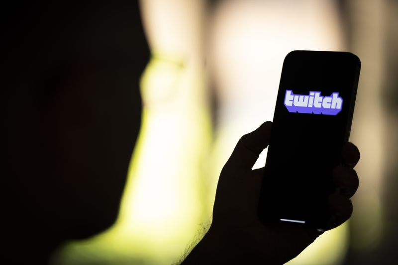 Silhouette of a person holding a smartphone with the Twitch logo on the device