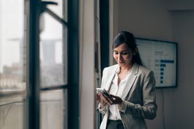 Woman in business attire looking down at a mobile phone.