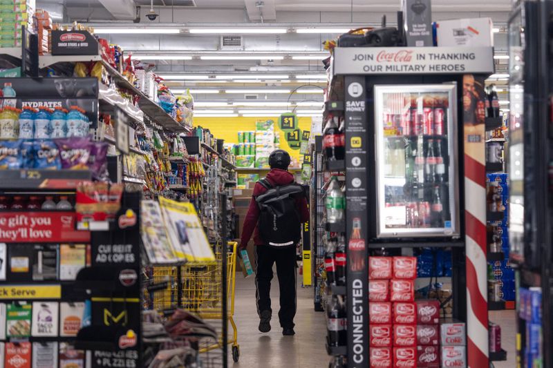 Person walking down an aisle in a store, surrounded by shelves of products and a Coca-Cola display in the foreground